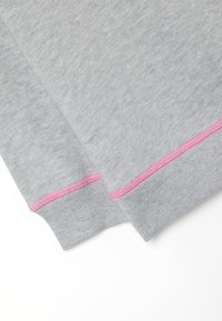 Tejido de sudadera gris con puños de canalé, con costuras en contraste en color rosa. Textura suave y diseño casual, doblado en los bordes.