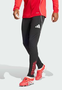 Athletic black leggings with a white Adidas logo, red side stripes, and a fitted design. Paired with red and white soccer cleats.