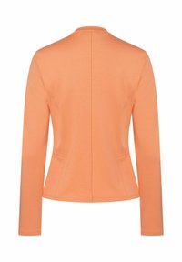Veste à manches longues pêche avec un design ajusté, col rond, en tissu de coton lisse, et poches latérales. Présente des coutures épurées et minimalistes.