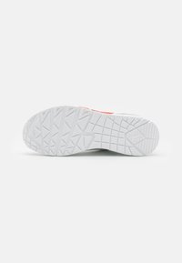 Suela de zapato en goma blanca con un patrón texturizado. Presenta surcos profundos y un pequeño acento rojo en el costado como detalle adicional.