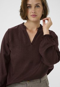 Blusa borgogna con scollatura a volant e polsini elasticizzati, caratterizzata da una vestibilità comoda e un tessuto testurizzato per un tocco di dettaglio in più.
