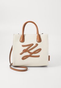 Kanvas håndtaske i cremefarvet med brune læderdetaljer. Har et forhøjet brunt logo design og korte håndtag samt en aftagelig skulderrem.