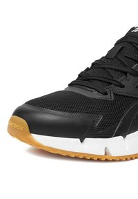 Juodas sportinis batelis su tinklinio viršumi, guminės apsaugos antikampiu ir baltu padu su tekstūruotu rudos gumos išoriniu padu.