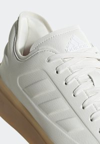 Vita sneakers med en texturerad läderöverdel, off-white snören och beige gummisula. Har präglade ränder och varumärkeslogotyp.