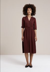 Abito borgogna con scollo a V con bottoni, maniche a tre quarti, vita cintata e lunghezza midi, caratterizzato da un tessuto leggermente texture.