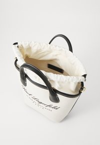 Kangas kott, millel on nööriga sulgemine, mustad nahkistmed ja trükitud logo. Kreemivärvi koos kontrastsete tumedate aktsentidega.