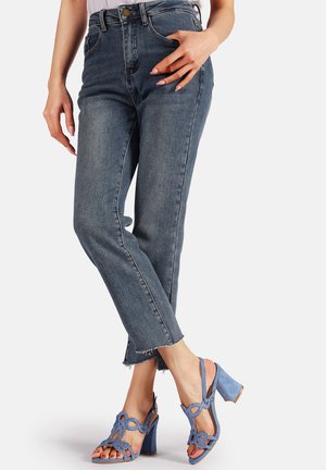 Jeans in denim blu scuro a vita alta con gamba dritta e orlo sfilacciato, abbinati a sandali con tacco blu chiaro caratterizzati da dettagli intagliati intricati.
