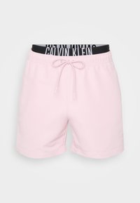 Helle rosa Schwimmhose mit einem elastischen schwarzen Bund, auf dem der weiße Schriftzug "Calvin Klein" steht. Sie verfügt über einen Kordelzug und einen glatten Stoff.