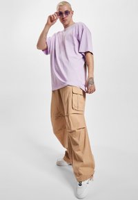 Loose-fitting lavender cotton t-shirt paired with beige cargo pants featuring side pockets and ankle zippers. Worn with white sneakers.