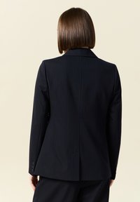 Blazer in fantasia a righe navy con vestibilità su misura. Presenta un colletto a scollo a V e tre bottoni su ciascun polsino. Tessuto liscio con una forma strutturata.