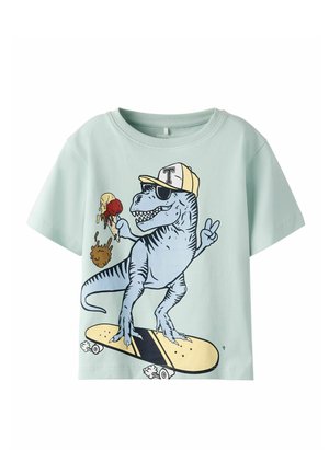 Light blue children's t-shirt with graphic of a smiling T-rex wearing a cap and sunglasses, holding melting ice cream, riding a skateboard, showing peace sign.