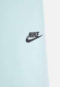 Vêtement en tissu bleu clair avec un logo Nike en noir. Le matériau semble lisse avec un léger éclat, mettant en avant un design simple et minimaliste.