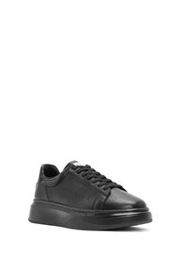 Zwarte lederen sneaker met dikke zool, vetersluiting aan de voorkant en kleine ventilatiegaatjes aan de zijkant, schuin naar links gepositioneerd op een witte achtergrond.