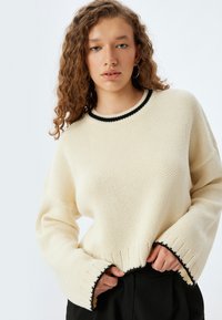 Maglione lavorato a maglia color crema con scollatura rotonda nera a coste, cuciture delle spalle scese e trim nero a contrasto lungo l'orlo e i polsini.