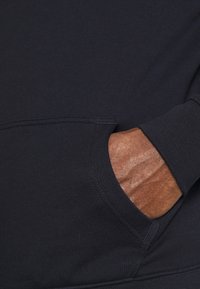 Sudadera negra de tela con un bolsillo en la parte delantera y puños acanalados. La tela parece suave, con costuras visibles a lo largo de las costuras.