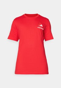 Camiseta de algodón roja con mangas cortas, cuello redondo y un logo blanco de "Predator" en el lado izquierdo del pecho. Textura suave y ajuste estándar.