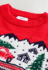 Red knitted sweater with a ribbed neckline, featuring a festive winter design of trees, houses, and a red truck on a white background.