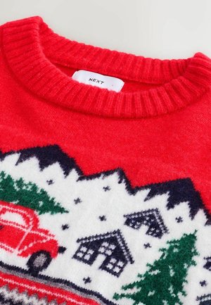 Rød strikket sweater med ribbet halsudskæring, der har et festligt vinterdesign med træer, huse og en rød lastbil på en hvid baggrund.