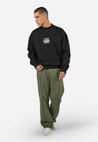 Czarna bluza z logo "PEGAADOR" w kolorze białym. Luźny krój, okrągły dekolt i ściągacze na rękawach. Połączona z oliwkowymi spodniami typu wide-leg i białymi sneakerami.