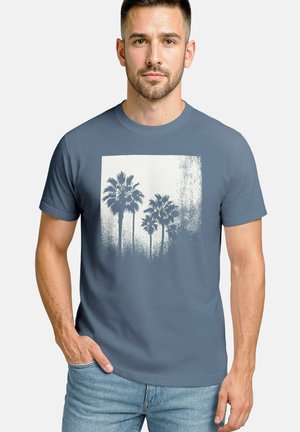 Blue cotton t-shirt featuring a white graphic of palm trees in a square pattern, displayed with a textured gradient background.