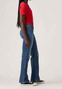 Haut rouge à manches courtes côtelé, associé à un jean flare bleu taille haute et des baskets noires à semelles blanches. Tissu lisse et coupe ajustée.