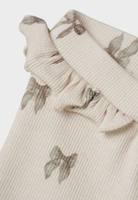 Tissu crème côtelé avec un col volanté, orné de motifs floraux discrets en gris et marron. Texture douce et détails délicats.