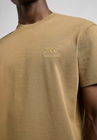 Khaki Baumwoll-T-Shirt mit Rundhalsausschnitt und kurzen Ärmeln. Es verfügt über ein strukturiertes Logo und eine "WORKWEAR"-Stickerei auf der linken Brust.