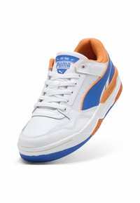 Zapatilla deportiva blanca con detalles en azul y naranja. Presenta cuero texturizado, cuello acolchado y una suela de goma con patrones de banda distintivos.
