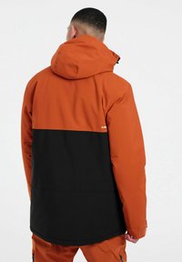 Orange und schwarze, farblich abgesetzte Jacke mit Kapuze, aus glattem, wetterbeständigem Material gefertigt. Mit einem Reißverschluss und verstellbaren Ärmelbündchen.