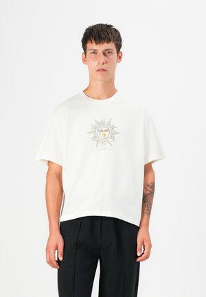 T-shirt en coton blanc avec un col rond, des manches courtes et un design graphique représentant un soleil et un visage au centre.