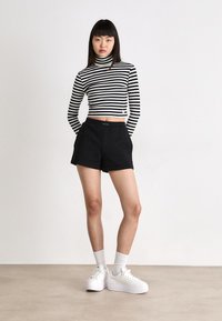 Pantaloni corti neri a vita alta abbinati a un maglione a collo alto cropped a righe bianche e nere. Le sneakers bianche con plateau e i calzini alla caviglia completano il look.