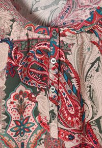 Blouse à motifs multicolores avec des designs en paisley rouge, turquoise et crème. Détails de bouton sur le devant avec un col rond.