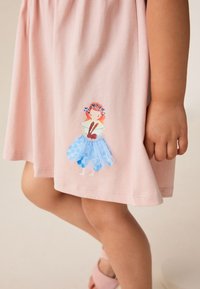 Roza obleka z modrim vzorcem z ilustracijo deklice z rdečimi lasmi in cvetjem. Mehka tkanina, enostaven dizajn, dolžina do kolen.