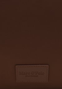 Sac en nylon brun avec une surface texturée, un patch logo en relief et des accents cousus. Fini lisse avec une forme rectangulaire contemporaine.