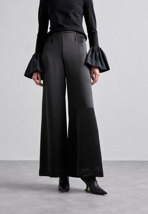 Μαύρο παντελόνι φαρδύ με ύφασμα λείο και γυαλιστερό, που διαθέτει ψηλή μέση και διακριτή γυαλάδα. Συνδυάζεται με μανίκια σε σχήμα καμπάνας.