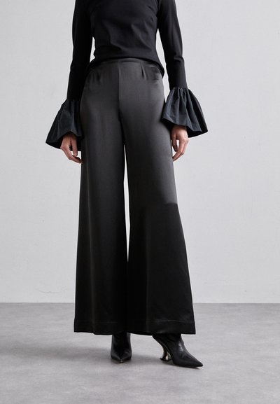 Pantalons larges noirs en tissu lisse et brillant, avec une taille haute et un éclat subtil. Associés à des manches en forme de cloche.