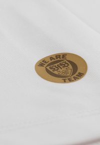 Tessuto bianco con una superficie liscia presenta un distintivo rotondo in oro con la scritta "SIAMO UNA SQUADRA" e un design a scudo.