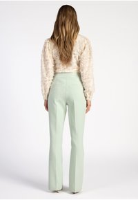 Lichtbeige, textuurachtige top met lange mouwen en volumineuze mouwen, gecombineerd met mintgroene, strak zittende broek met een gladde stof en uitlopende zoom.