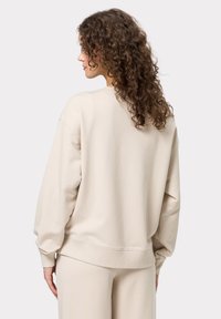 Felpa beige con vestibilità rilassata, scollatura rotonda e polsini a costine. Texture morbida e design semplice e minimalista.