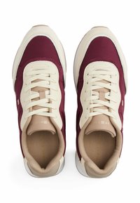 Burgundy and cream sneakers with a textured upper, featuring a rounded toe, laces, and a tan interior. White outsole with minimal branding.