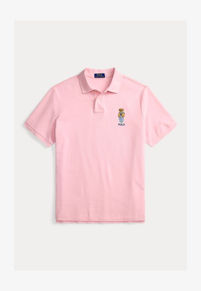 Lys rosa kortermet poloshirt med en liten brodert teddybjørn iført fritidsklær og teksten "POLO" på venstre bryst.
