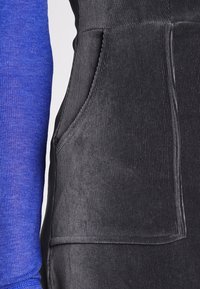 Närbild av en svart manchesterfick öra bredvid en blå långärmad ribbad ärm.