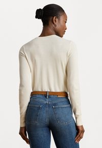 Maglione crema con maniche lunghe, colletto a coste e texture liscia, abbinato a jeans blu a vita alta e una cintura marrone.