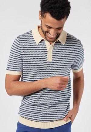 Polo de manga corta en color marino con rayas crema, que presenta un cuello crema y una tapeta de tres botones. Tela de punto texturizada con ribetes acanalados.