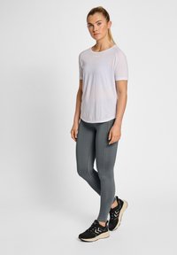Vit kortärmad träningsshirt, åtsittande grå leggings och svarta skor med beige detaljer. Slät textur, lätt material.