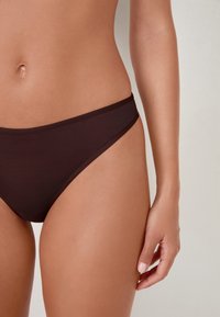 Bas de bikini marron en tissu lisse, avec une taille basse et un design minimaliste. Doté de fines lanières latérales et d'une finition sans couture.
