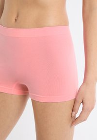 Pantaloncini corti in cotone rosa con una texture liscia e una vita ampia. Presentano un design aderente e aperture corte sulle gambe per il comfort.