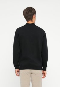 Sort crewneck sweatshirt med lange ærmer, lavet af et blødt stof. Har ribbede manchetter og talje, enkelt design uden mønstre.