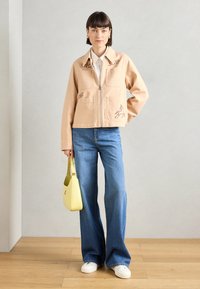 Μπέιτζ τζάκετ από τζιν με δύο μπροστινές τσέπες, κεντημένα σχέδια και φερμουάρ, συνδυασμένο με ανοιχτόχρωμες μπλε τζιν παντελόνες και κίτρινη τσάντα.