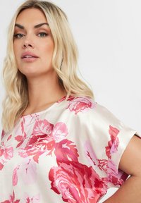 Kortärmad satinblus med ett blommönster i nyanser av rosa och rött på en krämfärgad bakgrund, med avslappnad passform och bred halsringning.